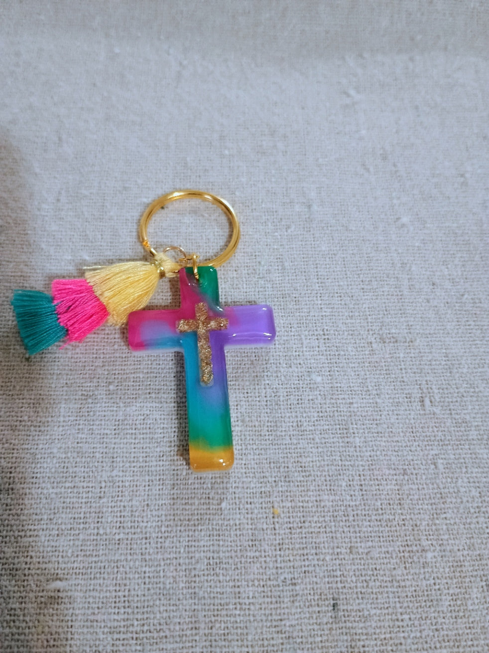 Colorful cross keychain with tassels on a textured gray background