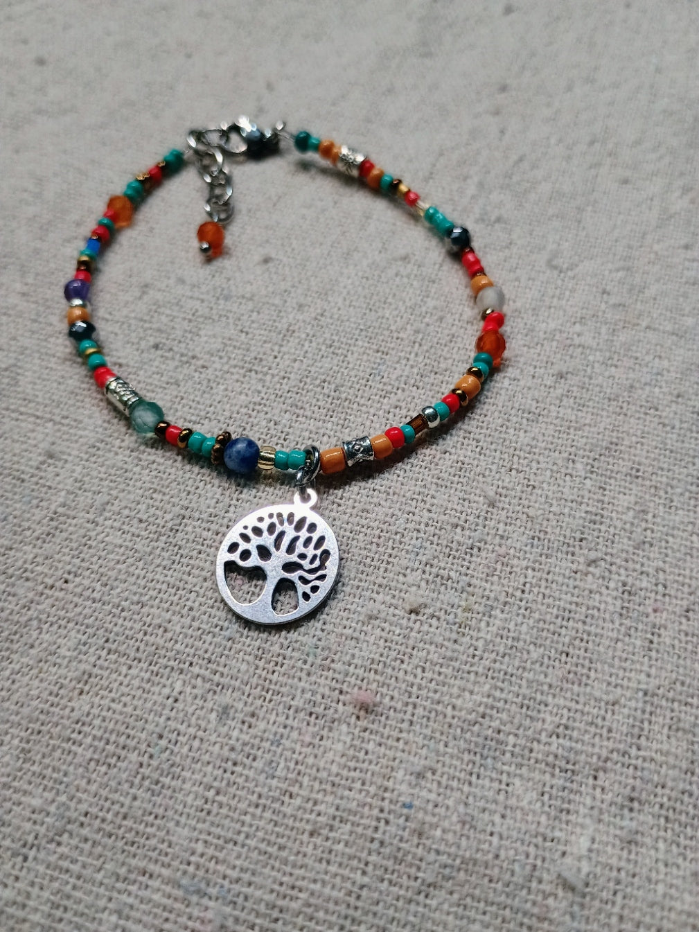 Colorful beaded bracelet with a tree of life charm on a textured surface