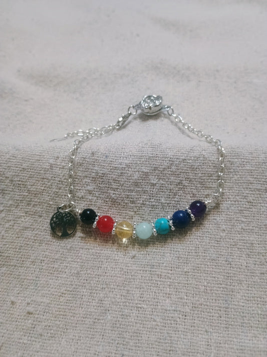 7 Chakra Bracelet with Tree of Life Charm on linen fabric, showing all seven gemstone beads and silver chain