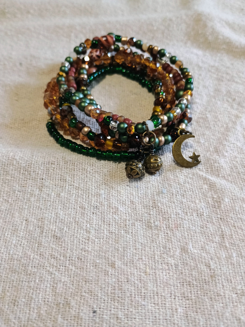 Six green, amber and burgundy beaded bracelets with brass-colored moon and round charms