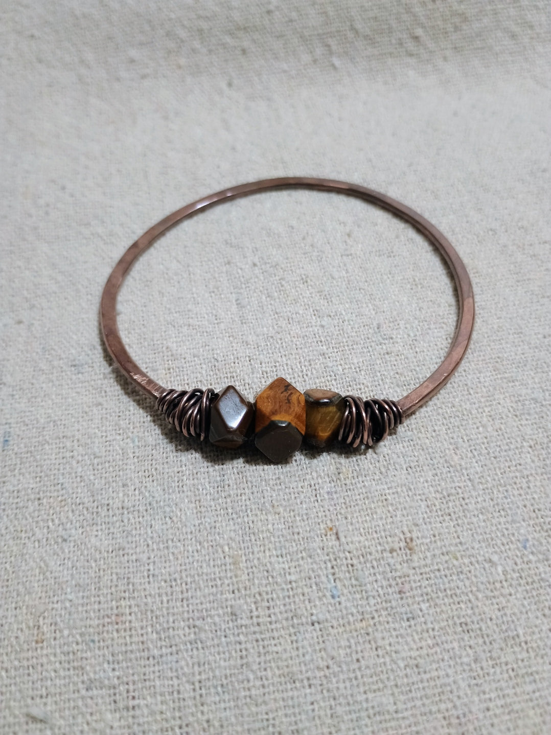 Bangle with irregular-cut golden-brown tiger’s eye stones, oxidized metal, and dark coiled accents on a light fabric background.