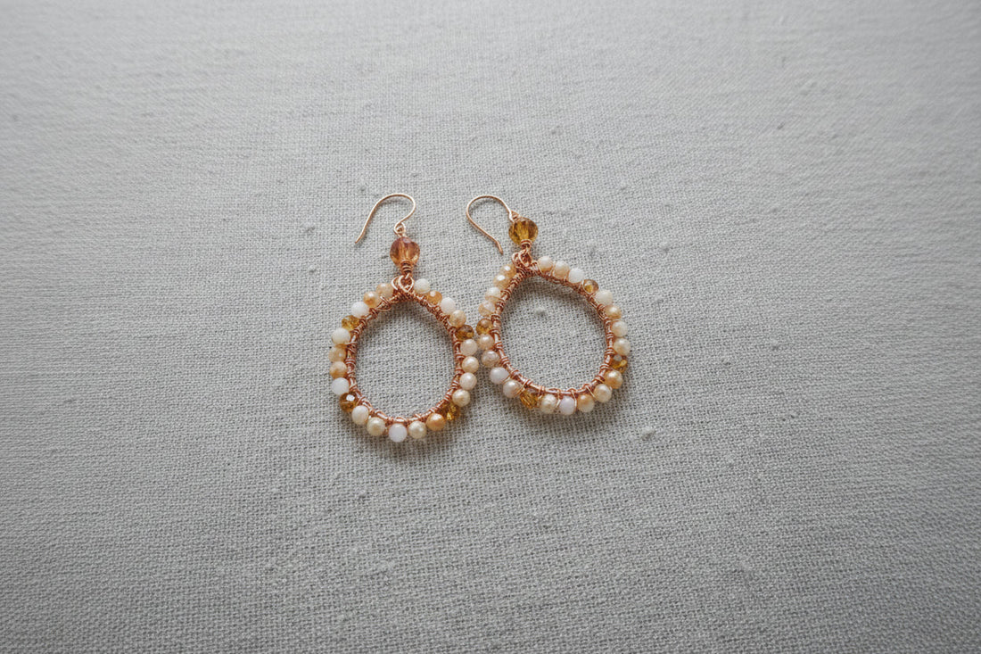 Handcrafted teardrop earrings with white and amber beads on gray fabric background