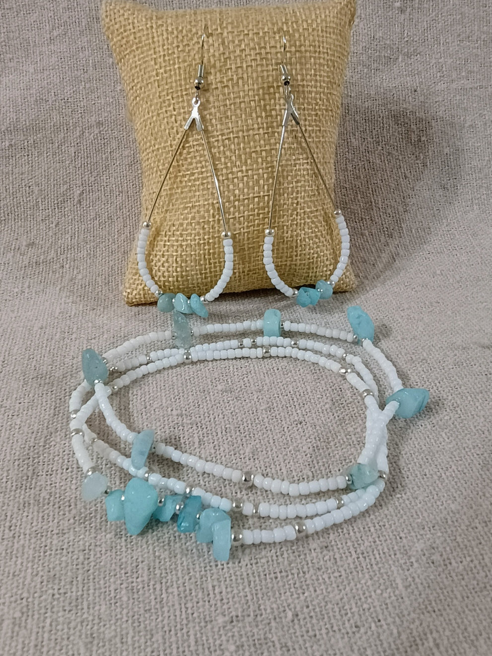 Close-up of a silver bead necklace with a teal heart pendant worn on a woman's neck over a navy V-neck top