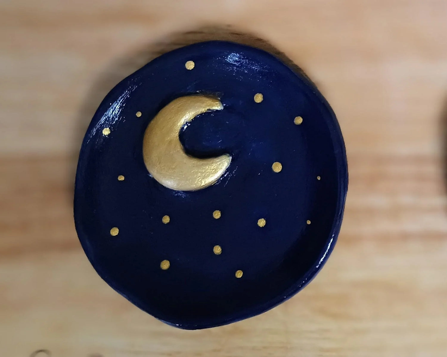 Handmade ceramic dish with navy blue glaze and gold crescent moon and stars design on wooden surface