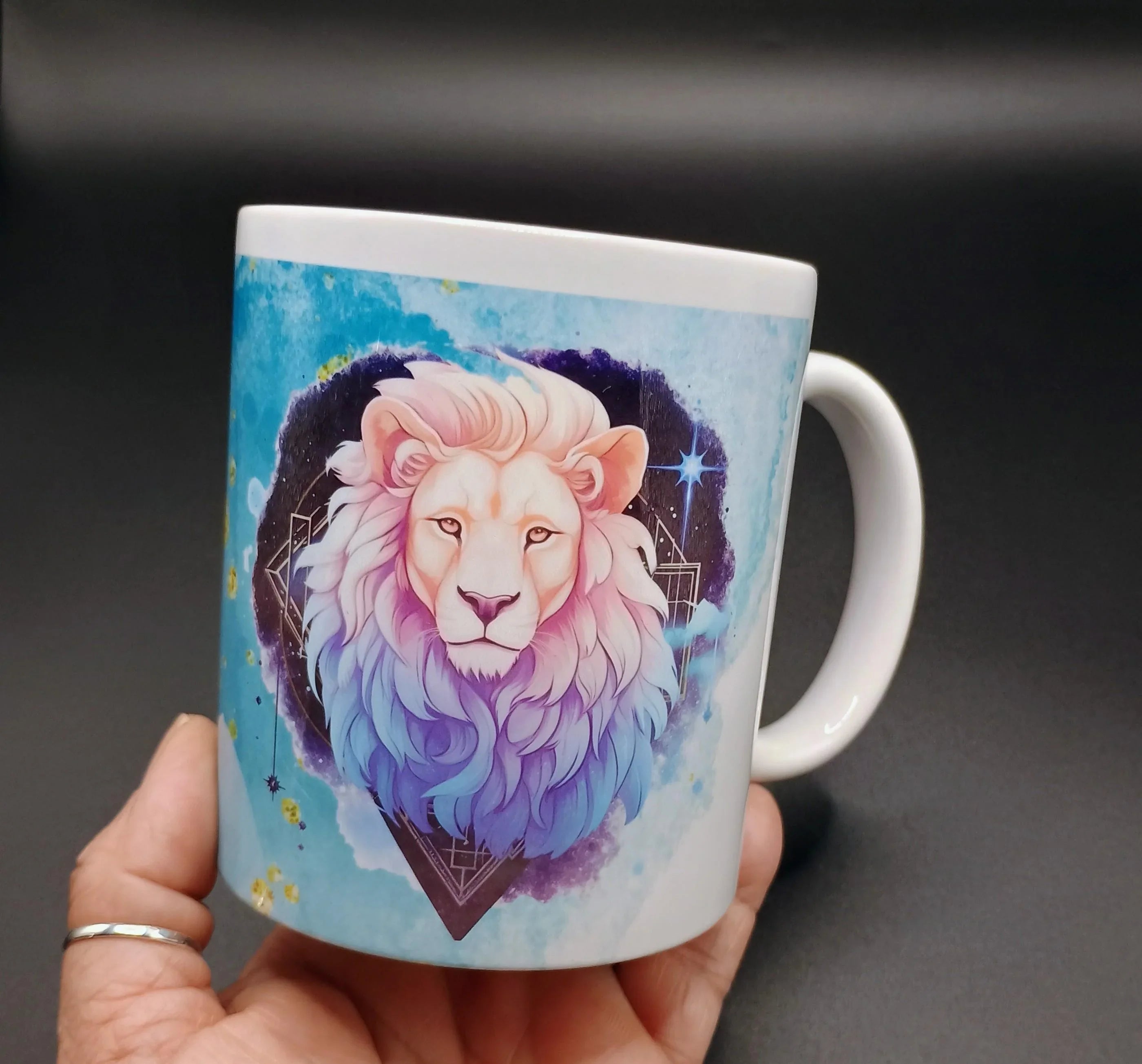 Hand holding white ceramic mug with colorful lion head art and blue cosmic background