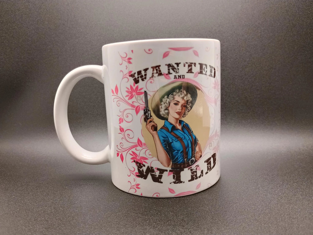 White coffee mug with vintage-style illustration of a woman cowboy holding gun and text 'Wanted and Wild'