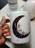 Hand holding white ceramic mug with black crescent moon and floral star pattern design