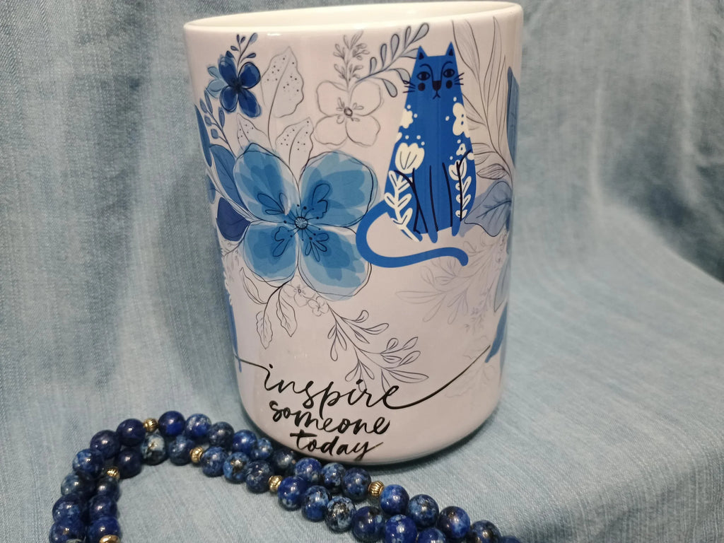 White ceramic mug with blue floral and cat design, inspirational text inspire someone today, blue beaded necklace