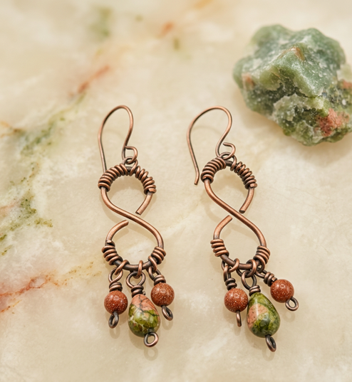 Copper-tone infinity dangle earrings with coiled accents, green and pink teardrop beads, and rust-colored round beads.