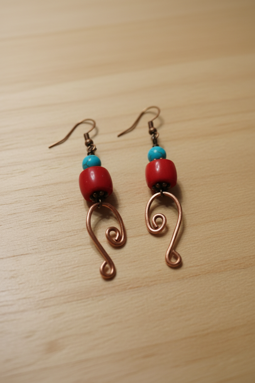 Copper scroll earrings with red coral and turquoise beads on wood surface