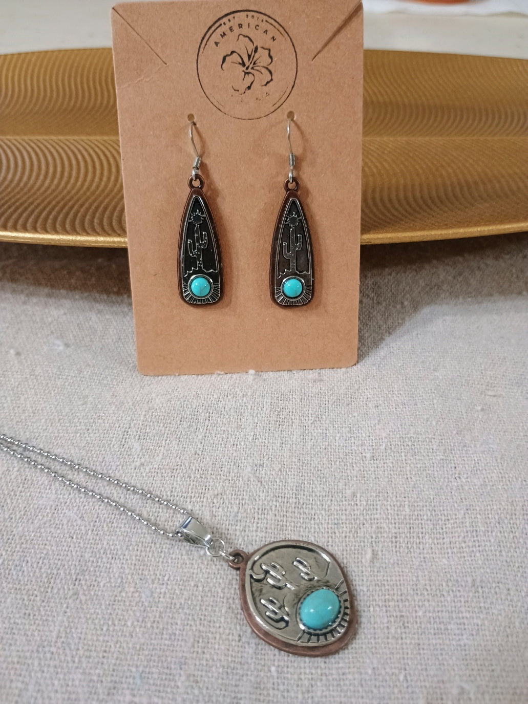 Handcrafted silver and turquoise earrings and pendant with cactus design on beige fabric and gold decor