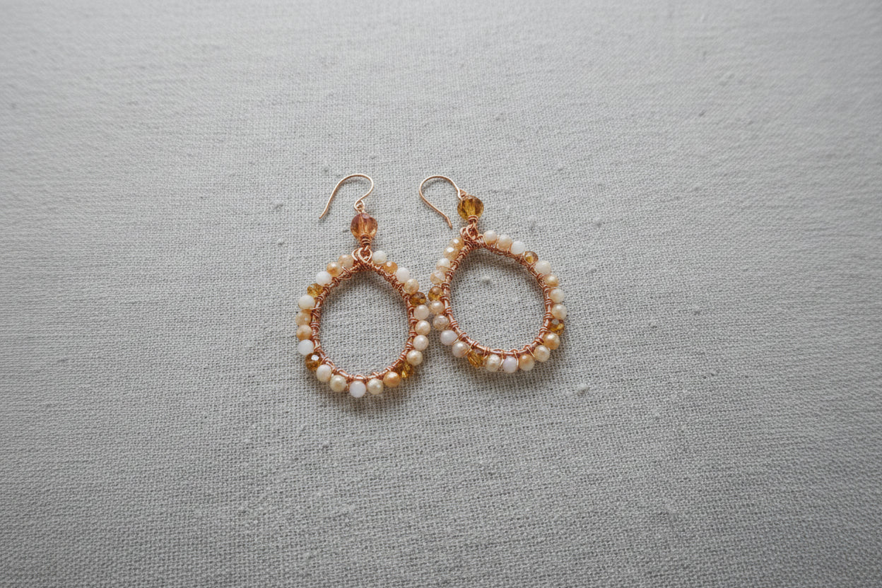 Handcrafted teardrop earrings with white and amber beads on copper wire on gray fabric
