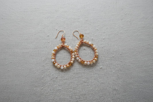 Handcrafted teardrop earrings with white and amber beads on copper wire on gray fabric
