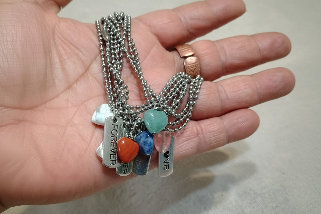 Hand holding multiple bracelets with various pendants on a neutral background