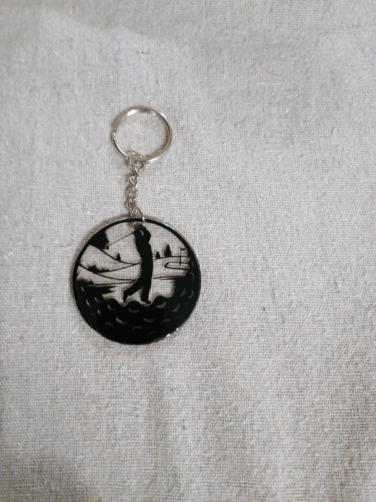 Keychain with a black and white design of a person playing golf on a gray fabric background