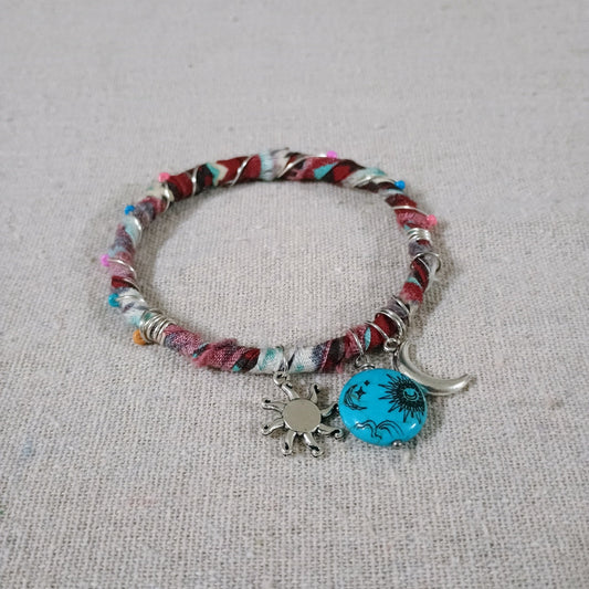Multicolored bracelet with sun and moon charms on a textured surface