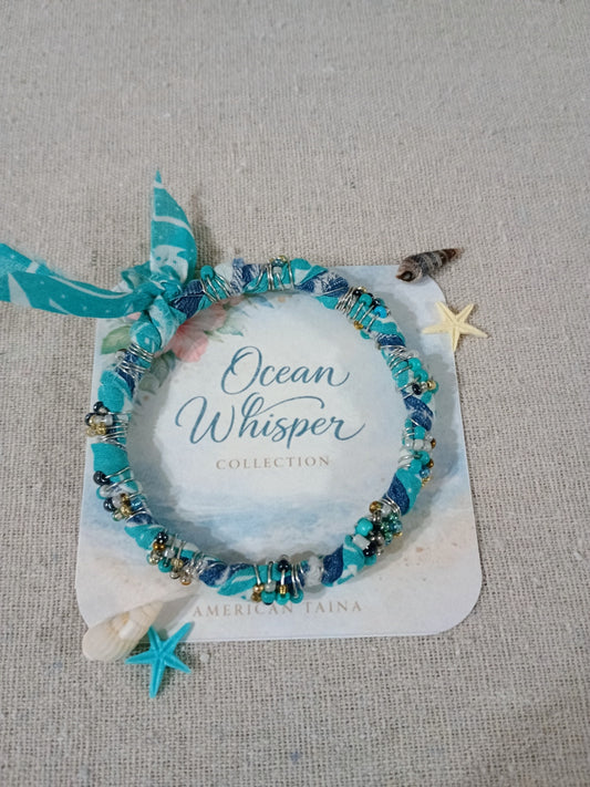 Blue beaded bracelet on a card with 'Ocean Whisper Collection' text, surrounded by starfish and a shell on a textured surface.