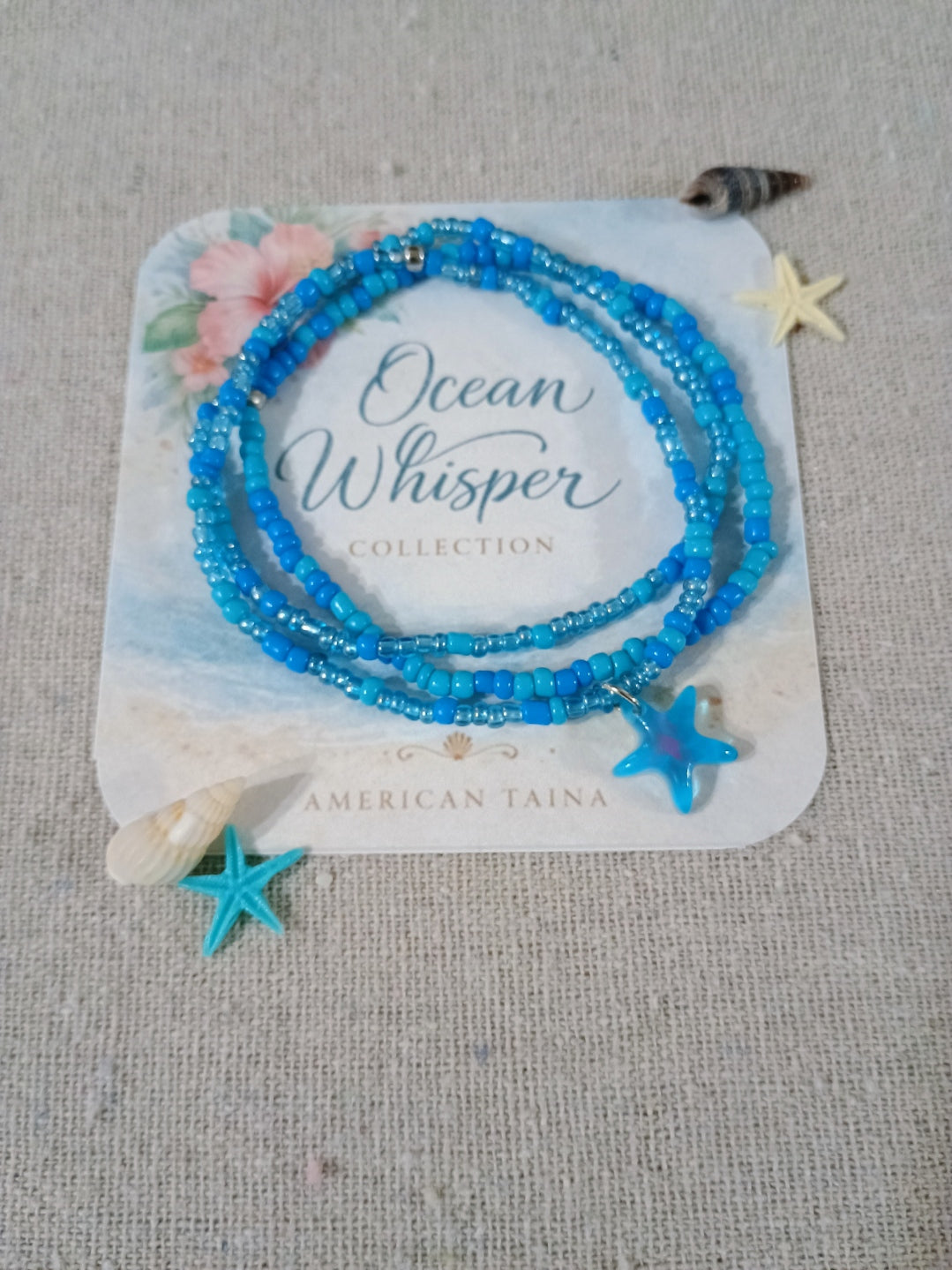 Blue beaded bracelet on a 'Ocean Whisper' collection card with starfish decorations.