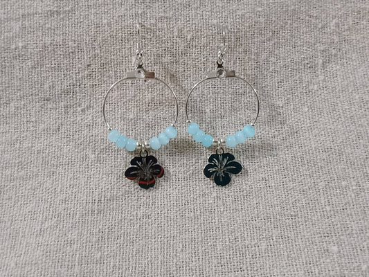 Pair of hoop earrings with floral charms and light blue beads on a textured fabric background