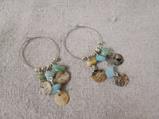 Hoop earrings with shell and bead charms on a textured fabric background