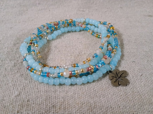 Stack of blue beaded bracelets with a silver charm on a textured fabric background