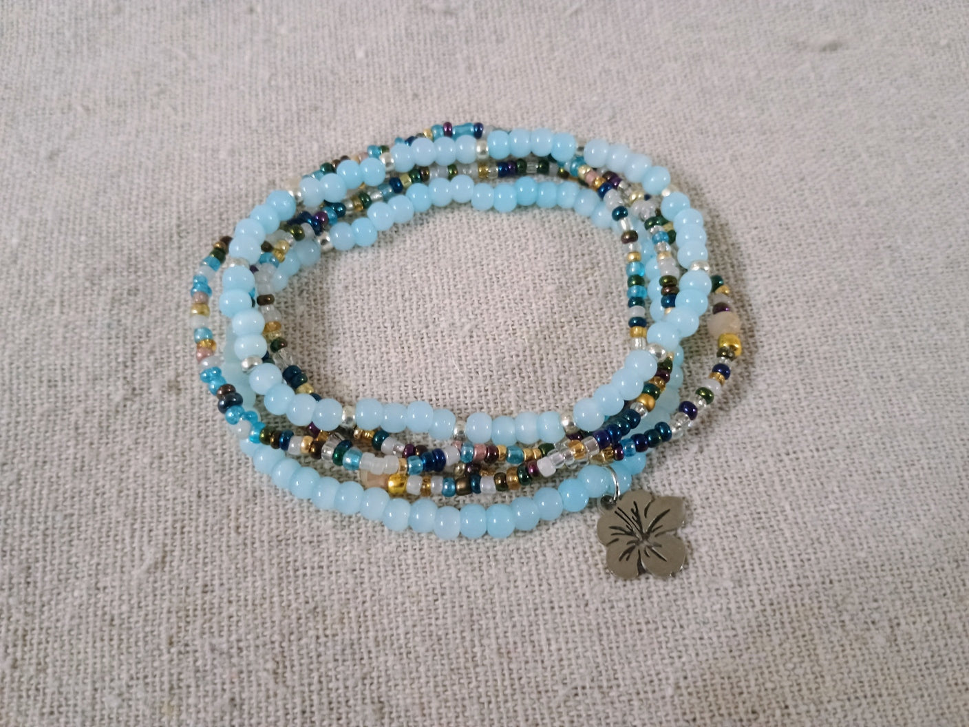 Beaded bracelet with a metal charm on a textured beige surface