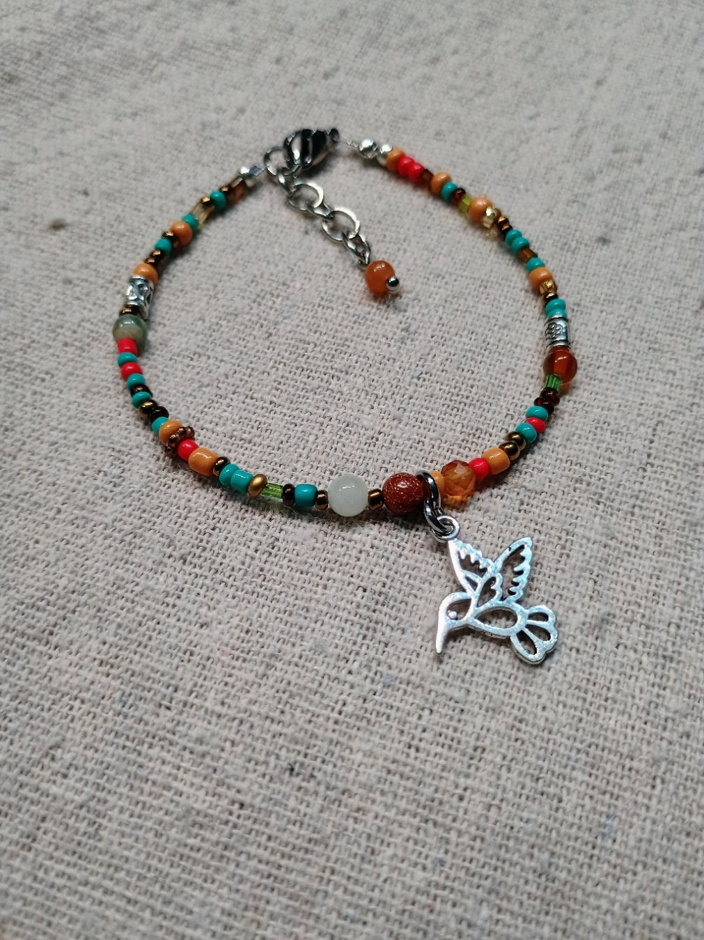 Colorful beaded bracelet with a silver hummingbird charm on a textured surface