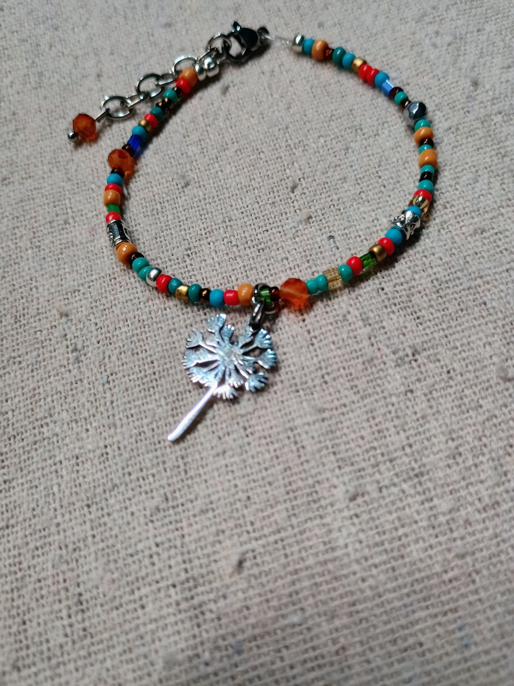 Colorful beaded bracelet with a silver dandelion charm on a textured surface
