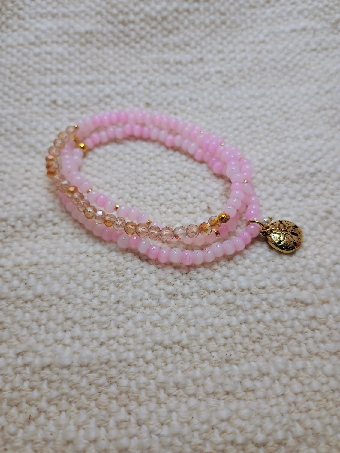 Pink beaded bracelet with a gold charm on a beige textured surface