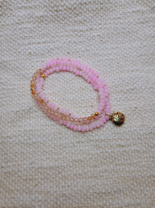 Pink beaded bracelet with a gold charm on a beige fabric background