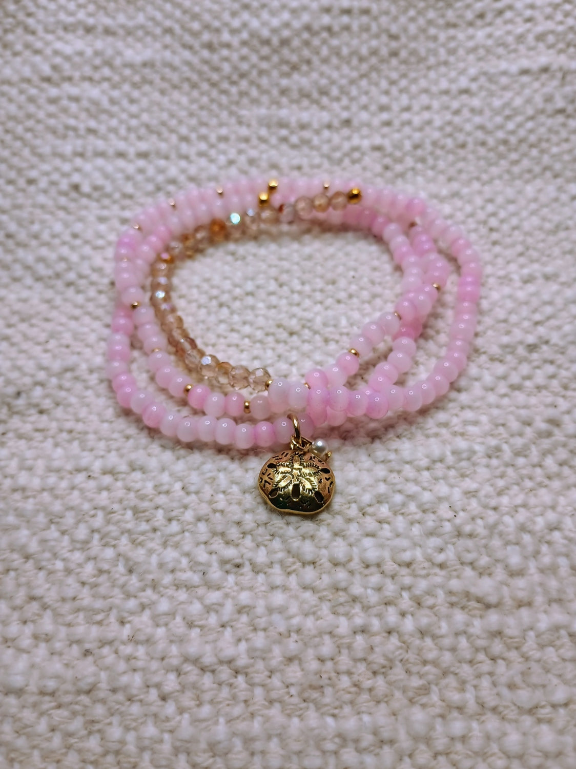 Pink beaded bracelet with a gold charm on a textured beige surface