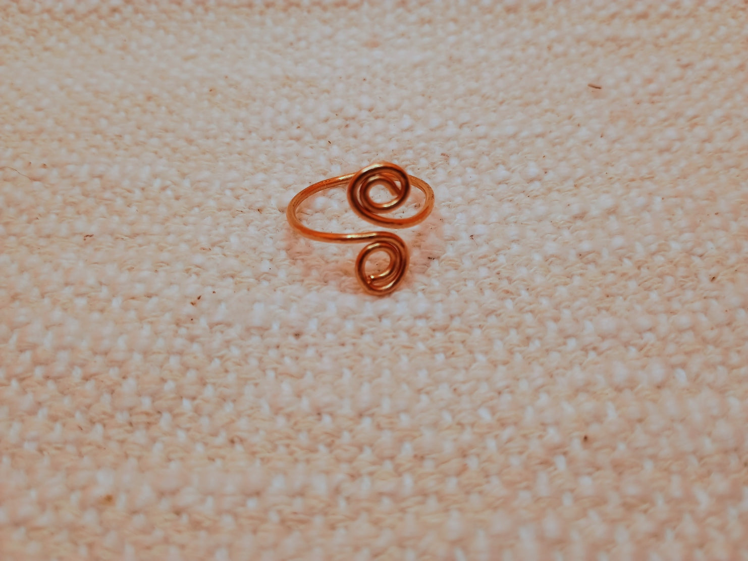 Handmade copper wire spiral ring on linen surface