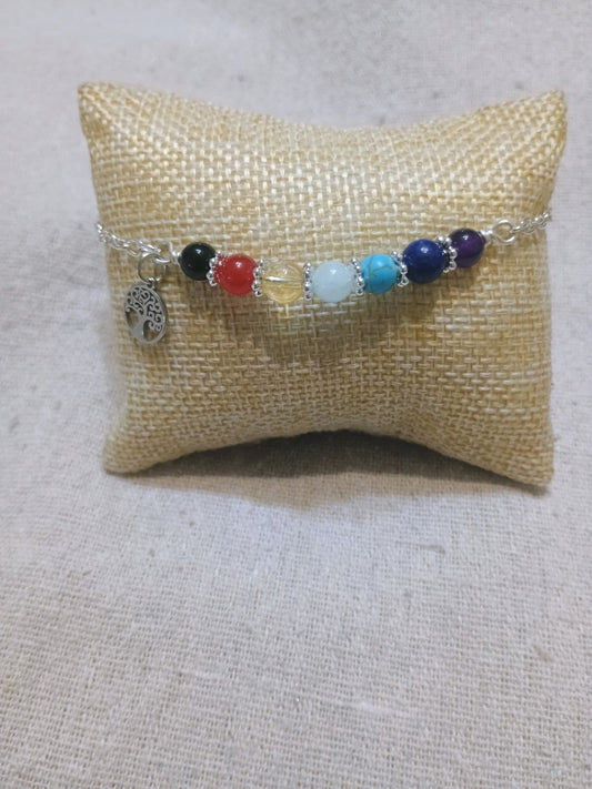 7 Chakra Bracelet with Tree of Life Charm displayed on a burlap pillow