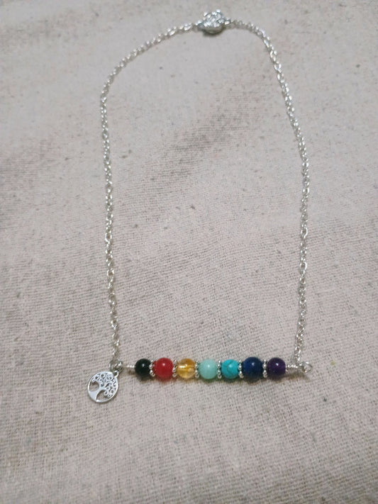 7 Chakra Bar Necklace with Tree of Life Charm laid flat on linen fabric