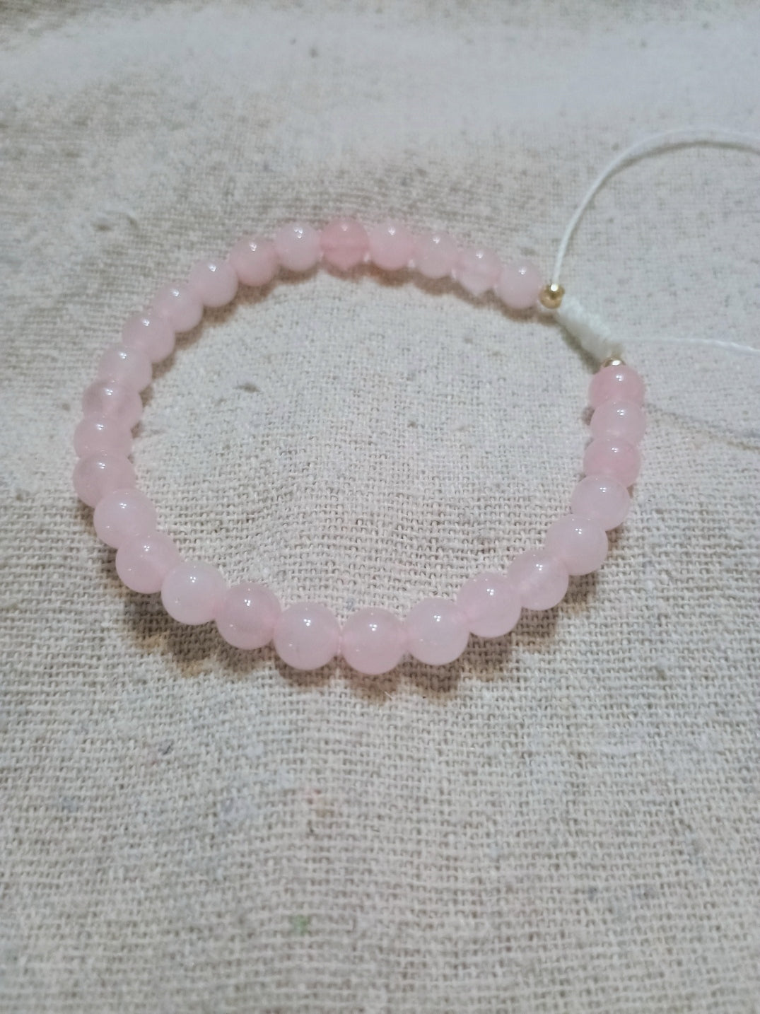 Handcrafted rose quartz bracelet on Brazilian wax cord, displayed on linen fabric