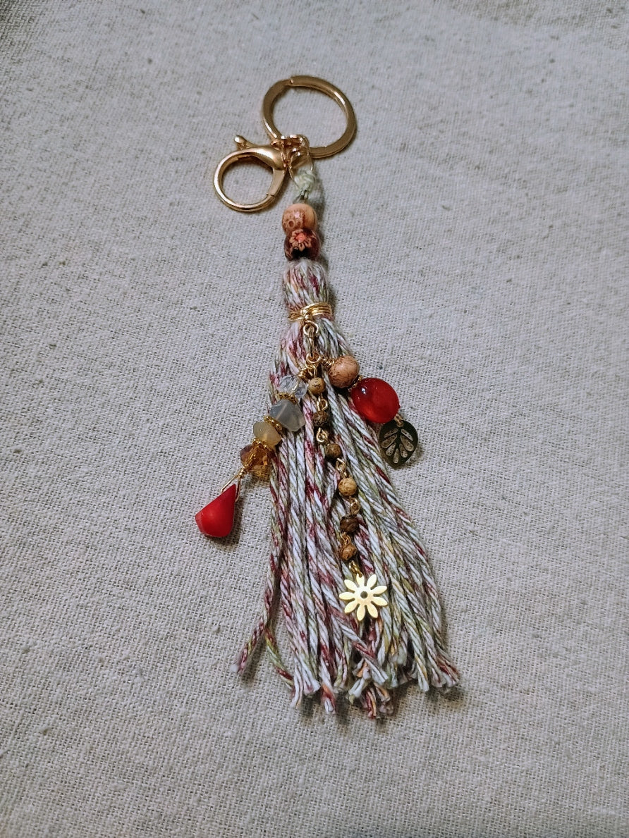Boho tassel charm keychain with red gemstone drops, gold daisy and leaf charms, mixed fiber tassel in cream burgundy and gray with gold-tone hardware
