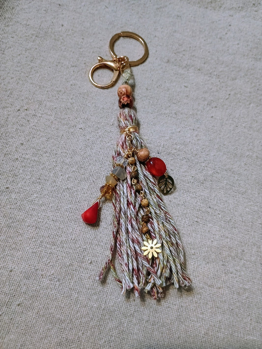 Boho tassel charm keychain with red gemstone drops, gold daisy and leaf charms, mixed fiber tassel in cream burgundy and gray with gold-tone hardware