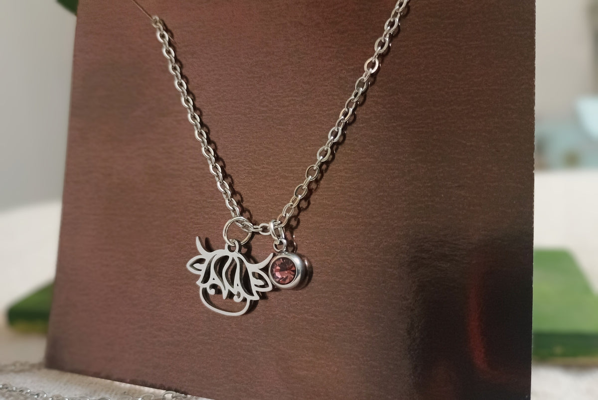 Silver-tone floral charm necklace with pink crystal accent on jewelry display card