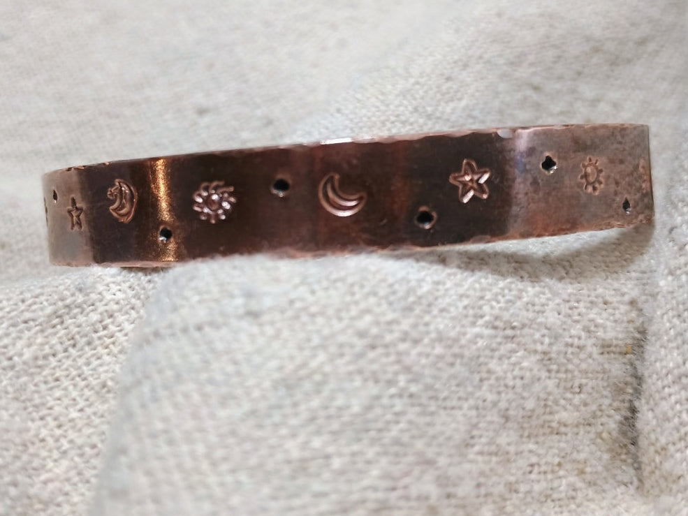 Front view of the handmade Celestial Harmony Copper Cuff showing its oxidized copper finish, celestial stamps and uneven hammered edges