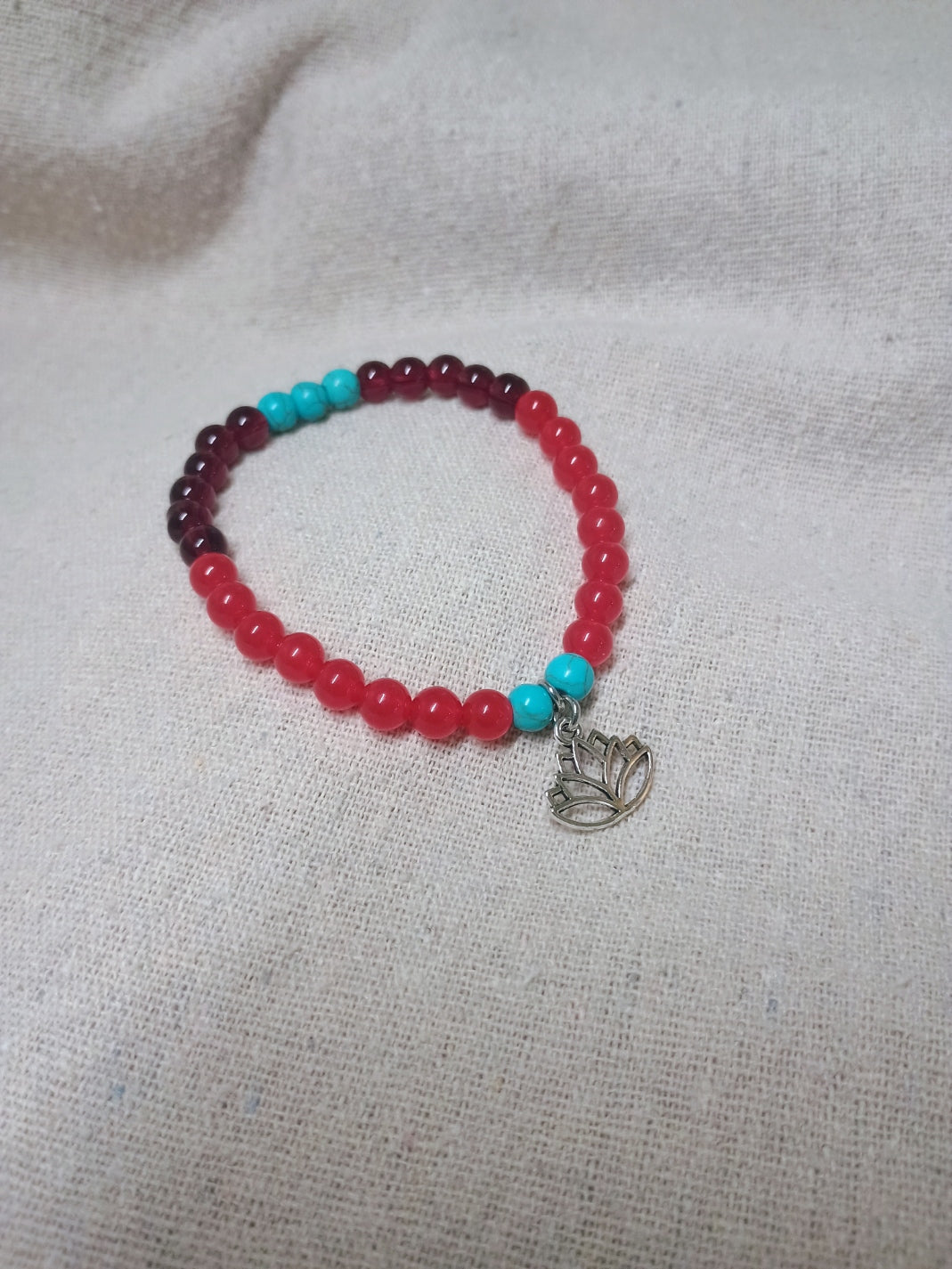 Red, burgundy and turquoise-colored beaded bracelet with lotus flower charm