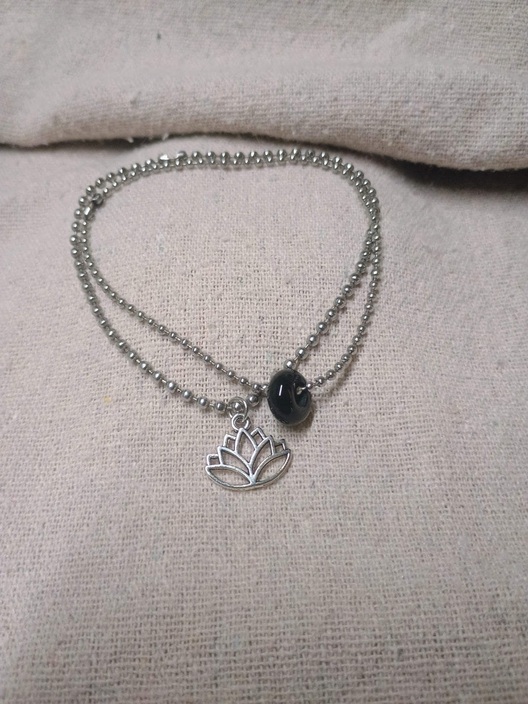 Two silver-tone ball-chain bracelets with a dark natural stone bead and an openwork lotus charm