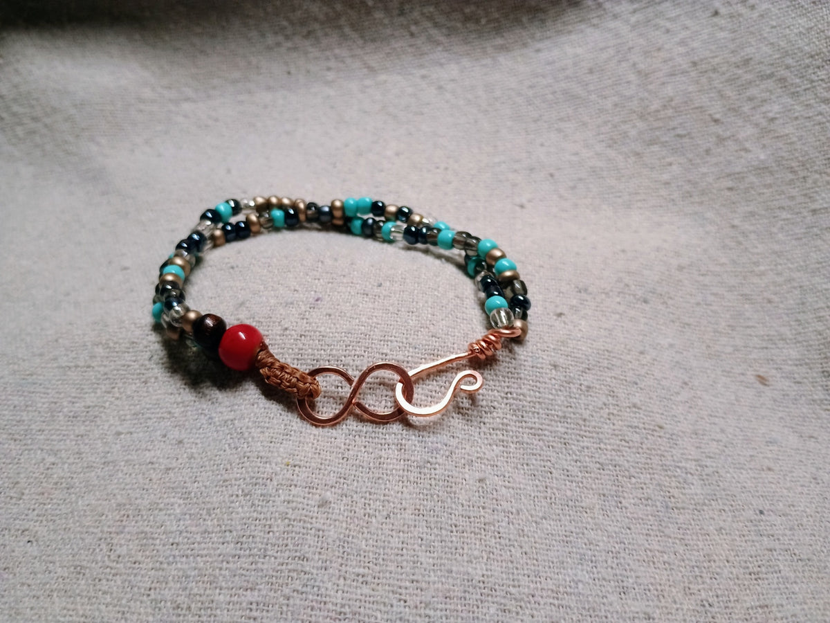 Earth and Ember boho bracelet with turquoise-colored and black beads, a red accent bead, and a copper-tone curved hook detail