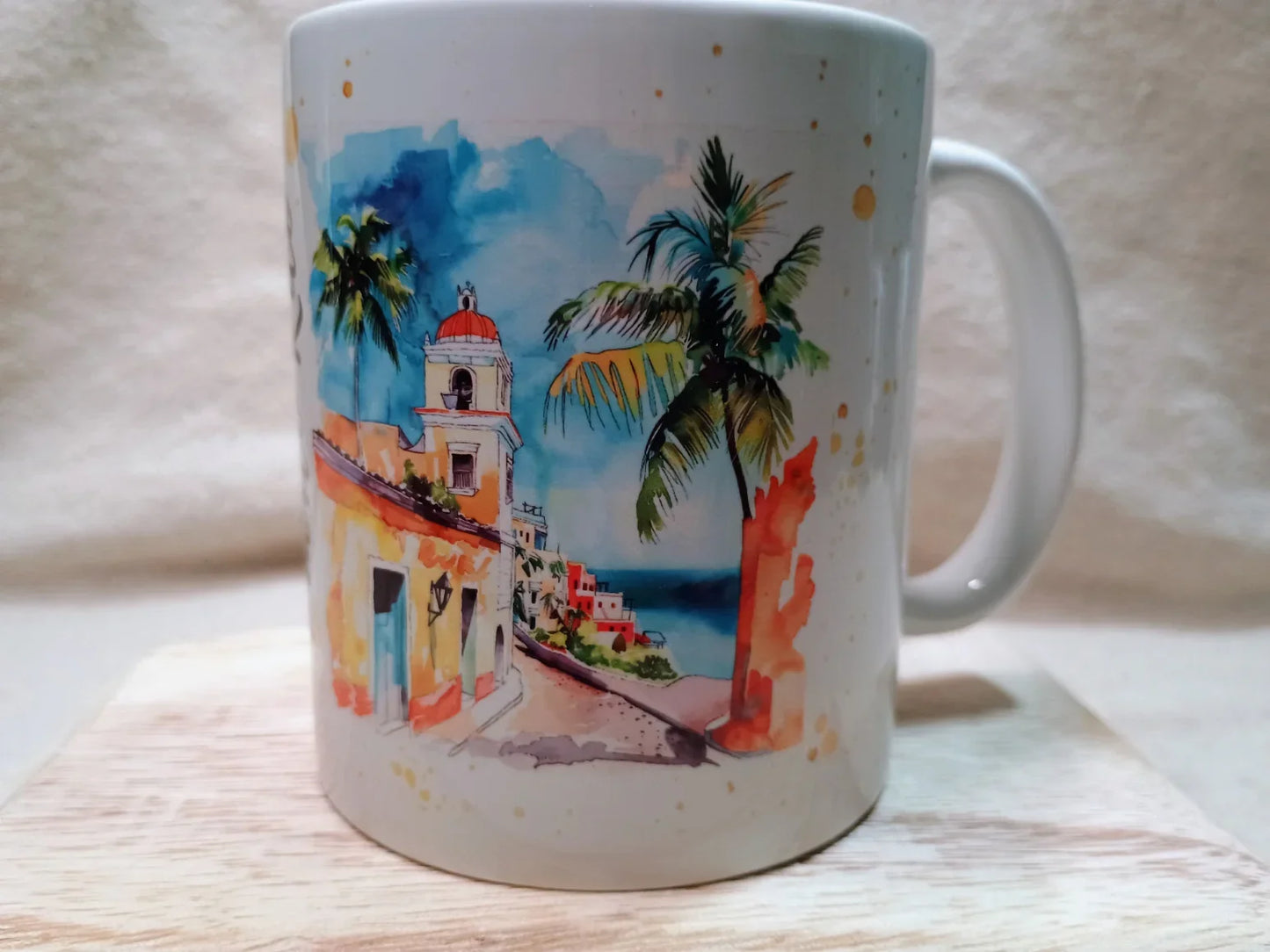 White mug with colorful watercolor illustration of coastal town, palm tree, and blue ocean
