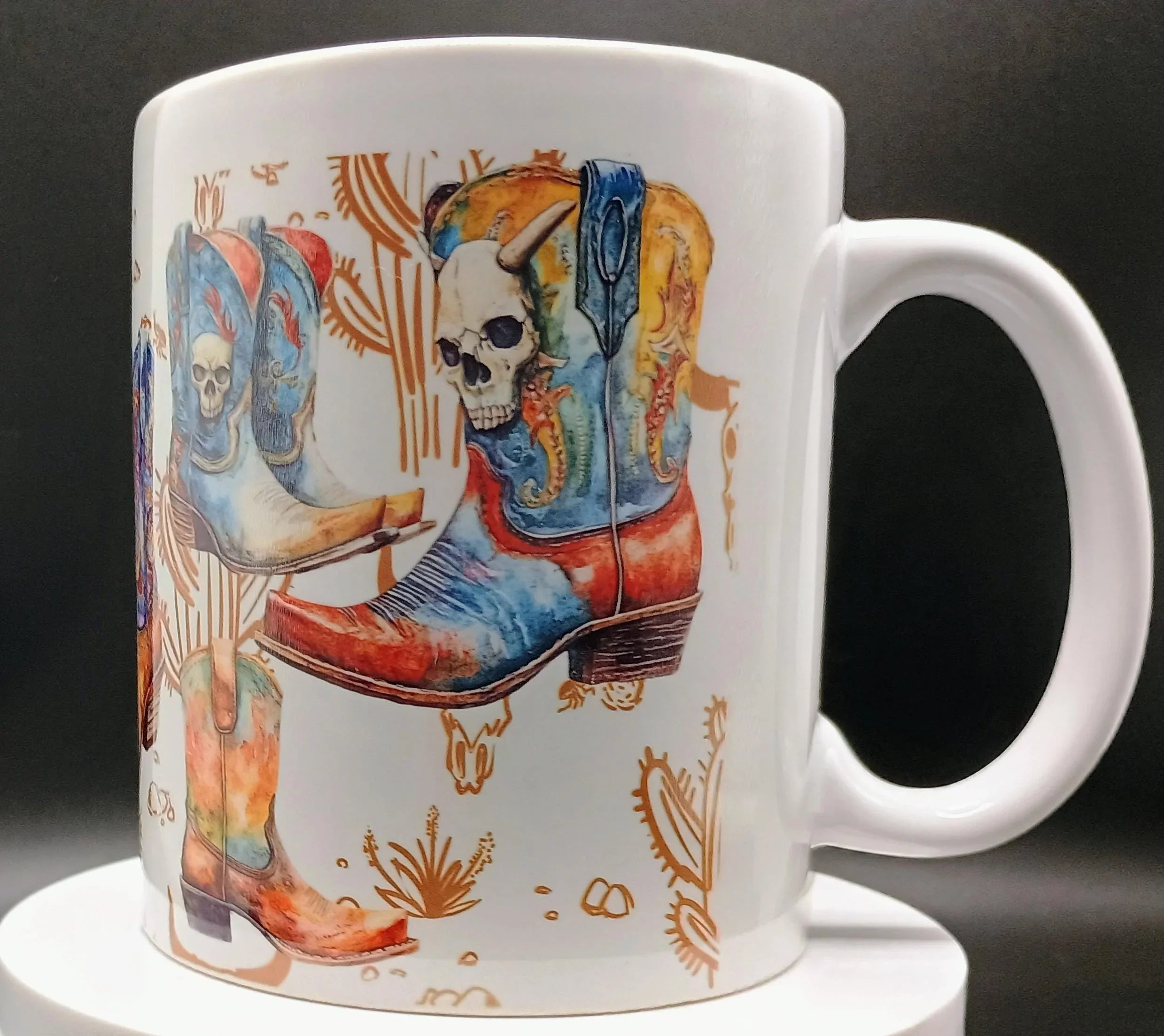 White ceramic mug with colorful cowboy boots and skull designs and desert-themed patterns