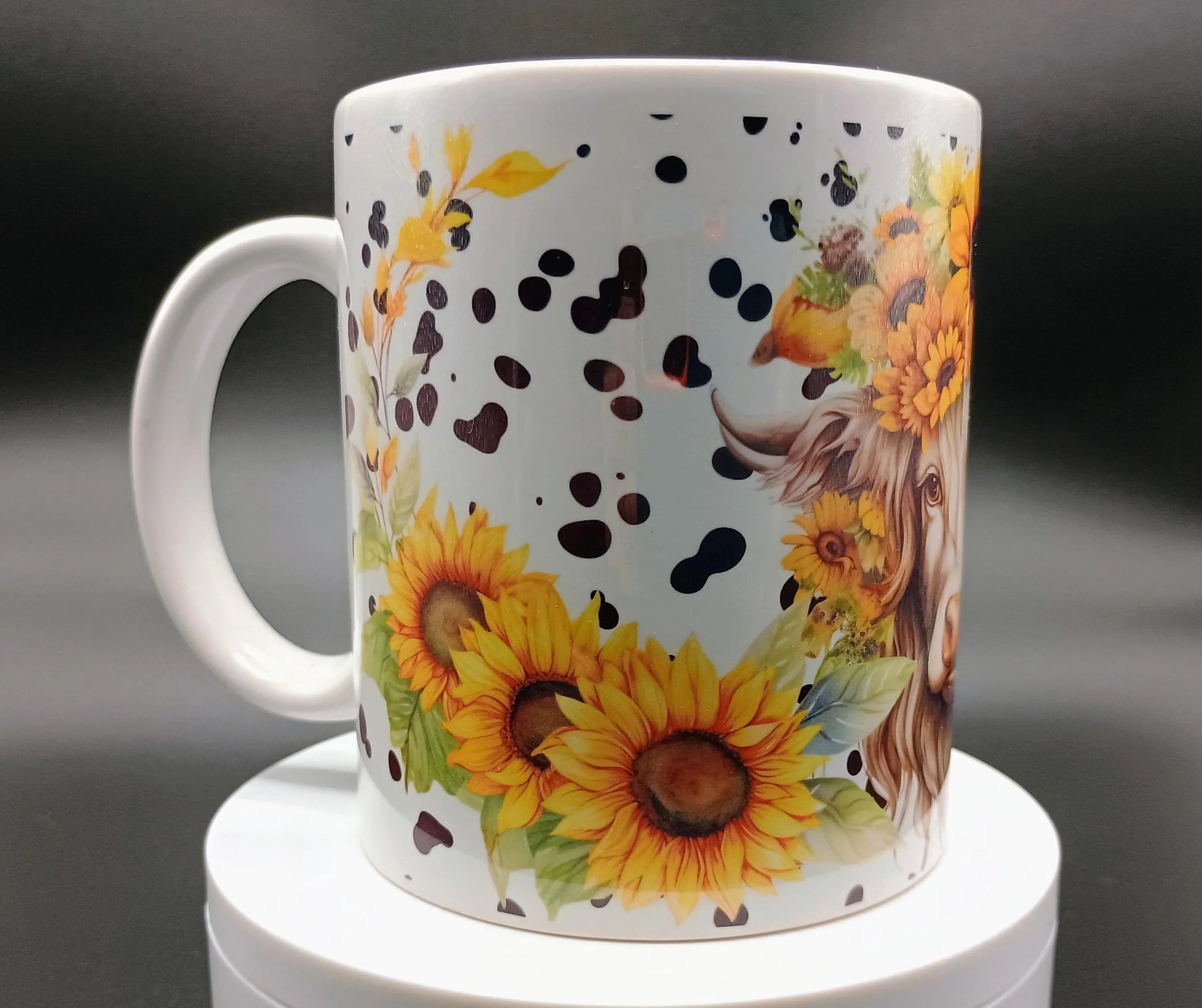 White ceramic mug with cow spots, detailed cow illustration, sunflowers, and small bird design