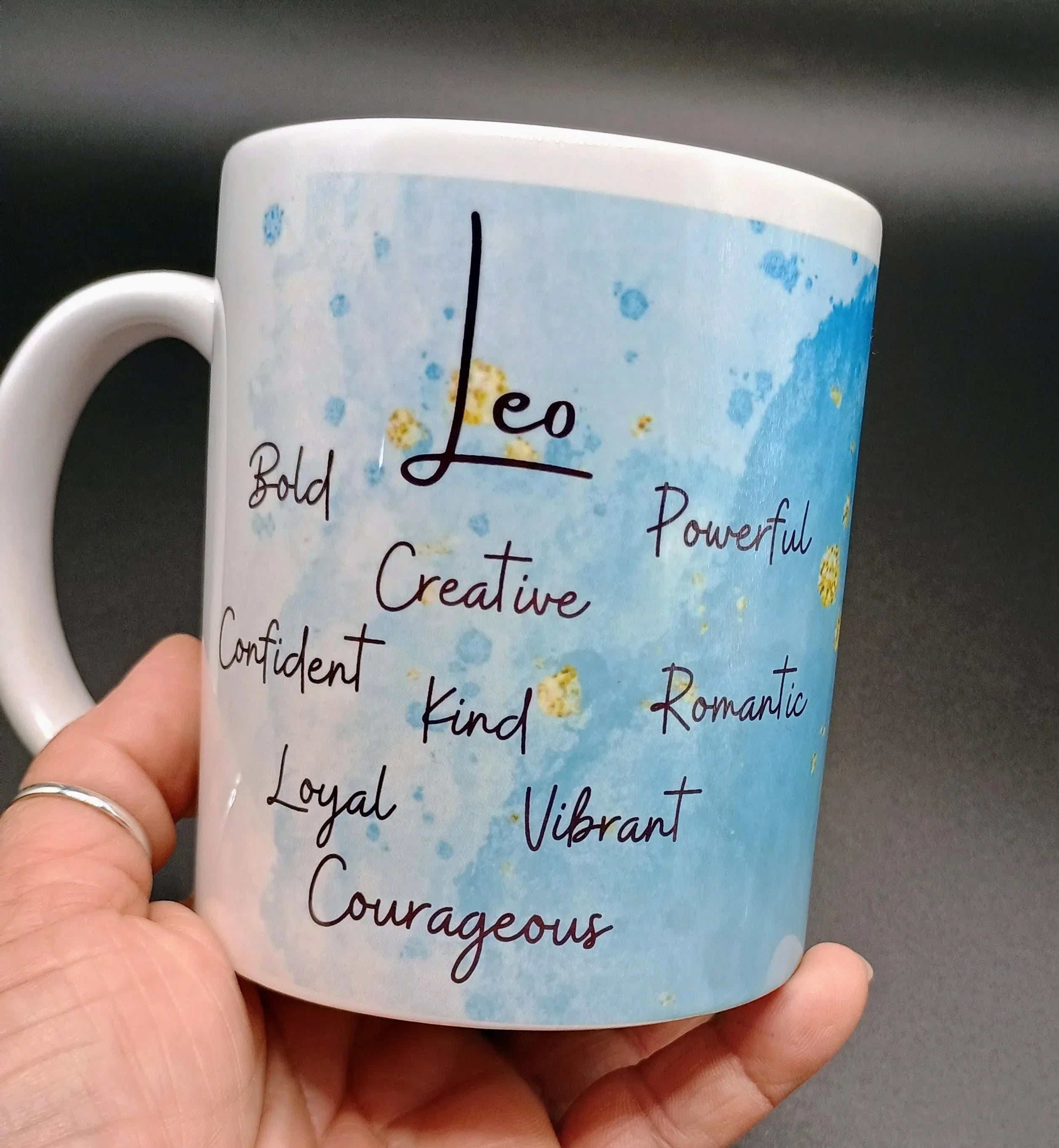 Hand holding white ceramic mug with blue watercolor background featuring Leo zodiac traits text