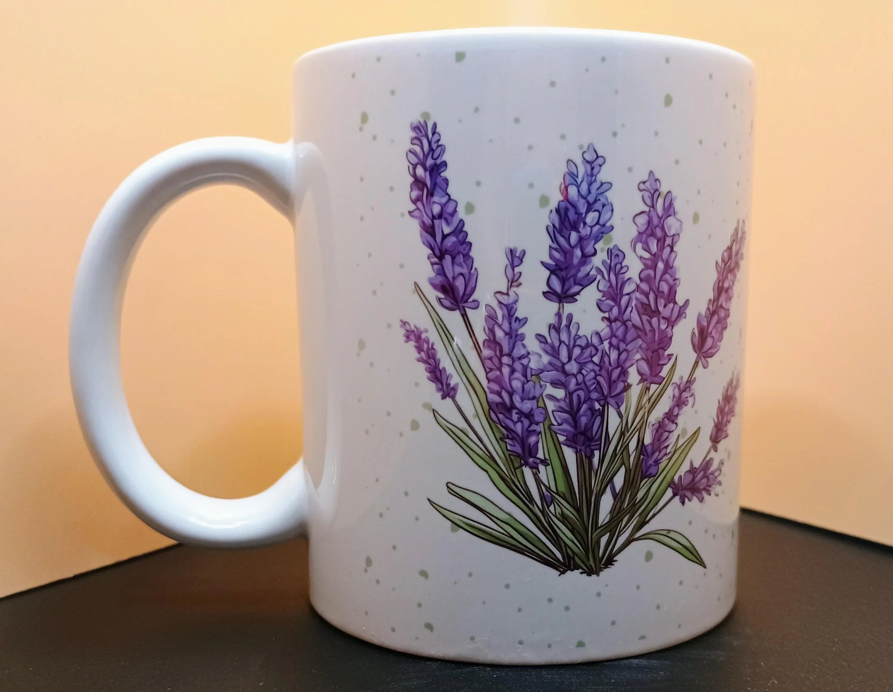 White ceramic mug with green speckles and purple lavender flower illustration on black surface