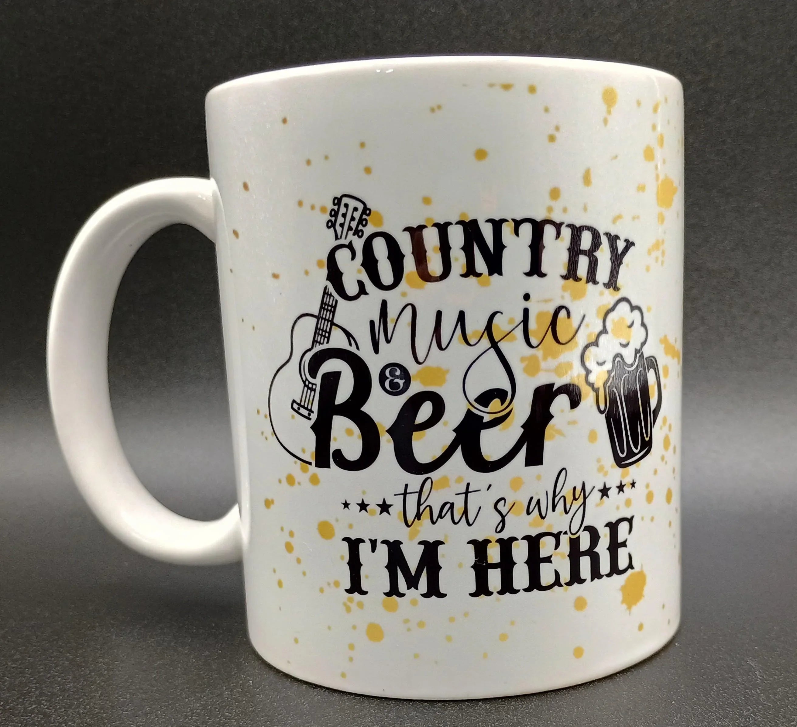White coffee mug with yellow splatter featuring text 'Country music & Beer that's why I'm here' with guitar and beer mug graphics