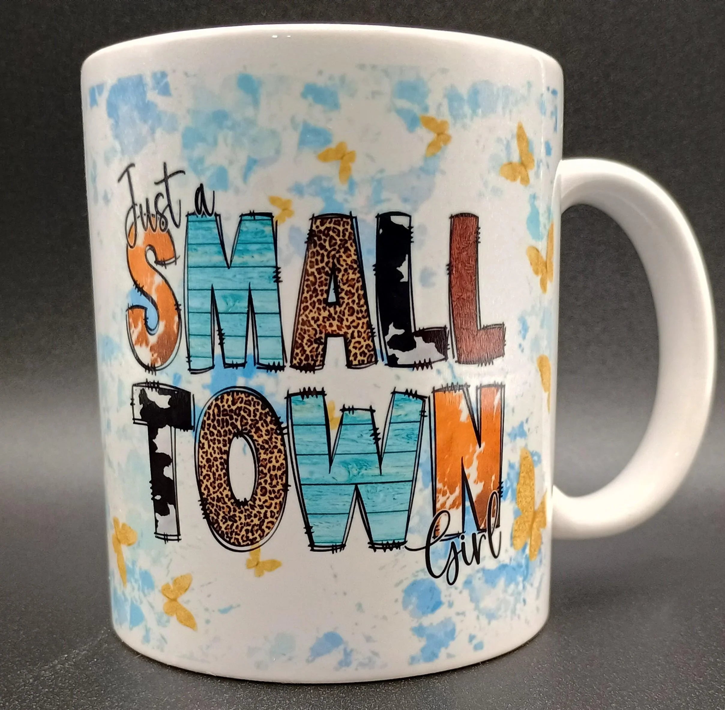 White ceramic mug with colorful text 'Just a Small Town Girl' and blue and yellow butterfly accents