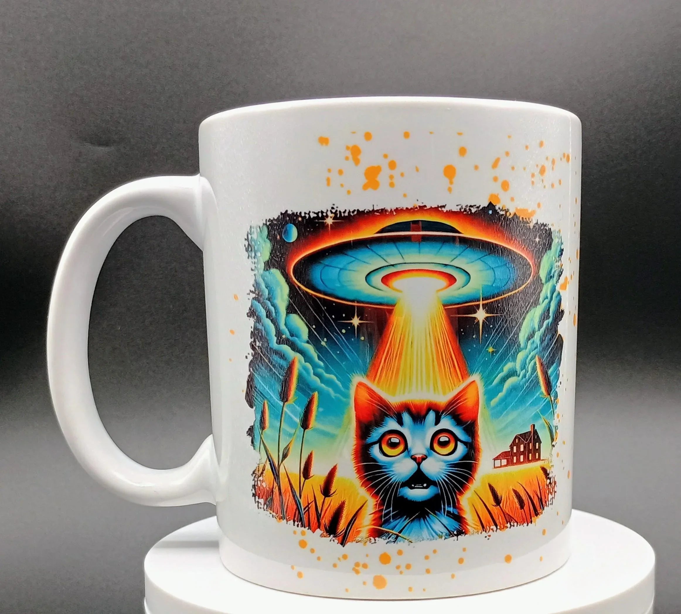 White mug with vibrant illustration of a wide-eyed cat under a glowing UFO beam in a field
